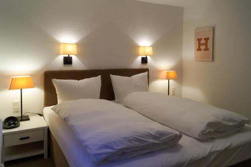 una camera con due letti con lenzuola bianche e due lampade di Hüs Claire a Kampen