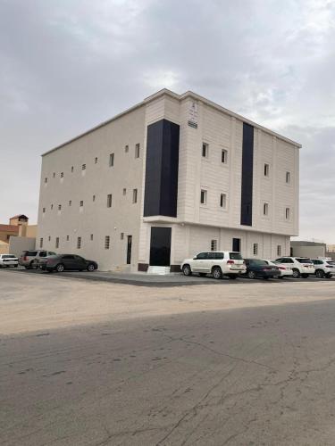 ein großes weißes Gebäude mit Autos auf einem Parkplatz in der Unterkunft شقة بغرفة وصالة in Hafar Al-Batin