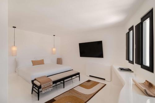 a white bedroom with a bed and a tv at Nobu Hotel Santorini in Imerovigli
