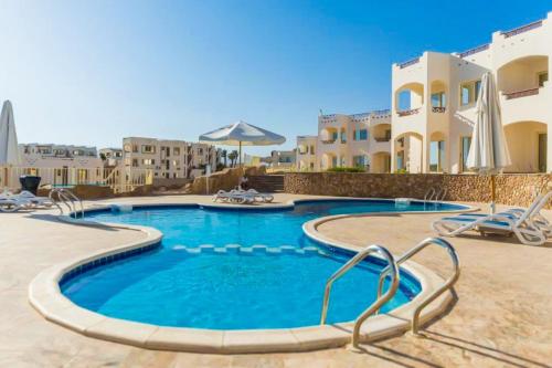 a swimming pool with chairs and buildings in the background at Sharks Bay Oasis Resort & Butterfly Diving Center in Sharm El Sheikh