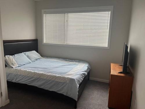 1 dormitorio con 1 cama, TV y ventana en Your Cozy Retreat, 2BR suite en Kamloops