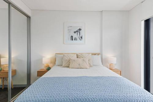 a white bedroom with a large bed with a blue comforter at Burelli Beach Escape - Breezy Seaside Charm in Wollongong