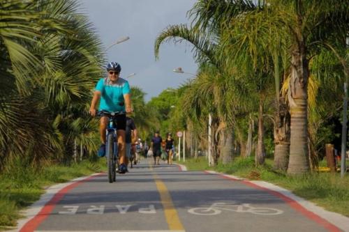 a man riding a bike down a road with palm trees at Casa de Praia Extremo Sul in Rio Grande