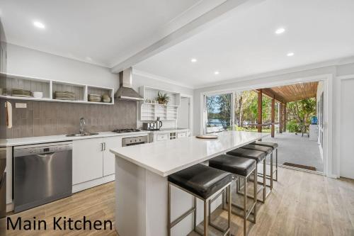 a kitchen with a large white counter and stools at Little Mirror Bay in Laurieton