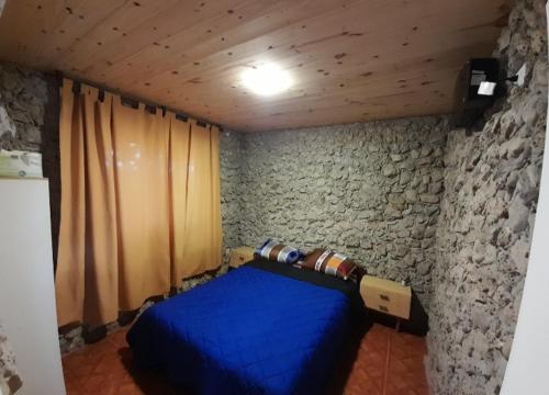 Un dormitorio con una cama azul y una pared de piedra en Alquiler playa Quequén en Quequén