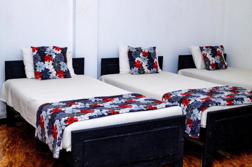 three beds in a room with red and black quilts at Sanasuma Hotel in Hambantota