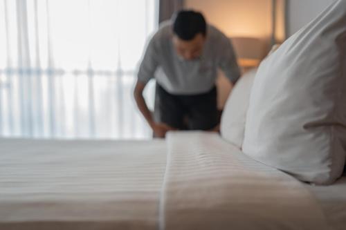 a man is standing next to a bed at The Capital Hotel Surabaya in Surabaya