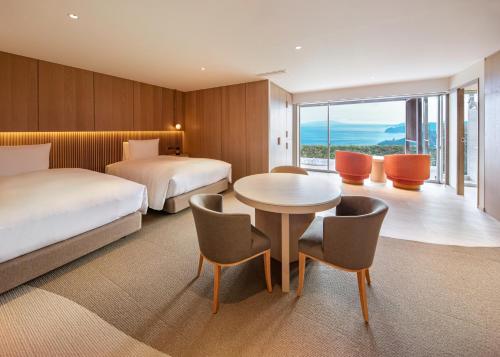 a hotel room with two beds and a table and chairs at Hotel Grand Bach Atami Crescendo in Atami