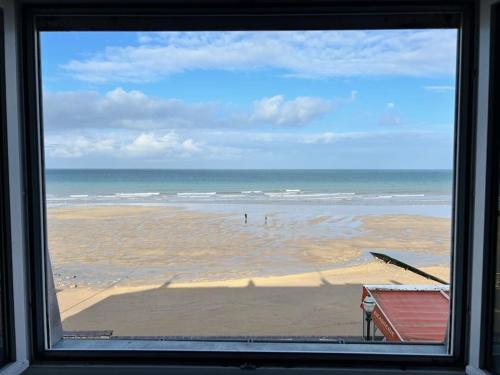 a window view of a beach with people in the water at L'Horizon - Duplex face à la Mer tout confort in Saint-Aubin-sur-Mer