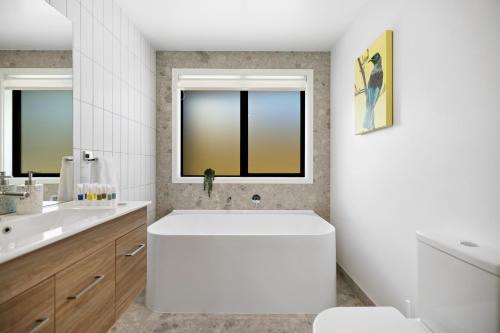 Baño blanco con bañera y lavamanos en Elite Holiday Homes - Remarkable Retreat, en Frankton
