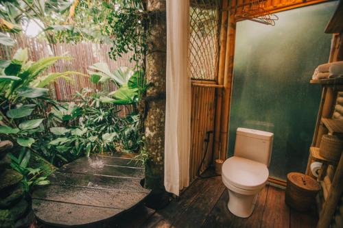 a bathroom with a toilet in a room with plants at Hideout Eco Bamboo House Bali in Selat