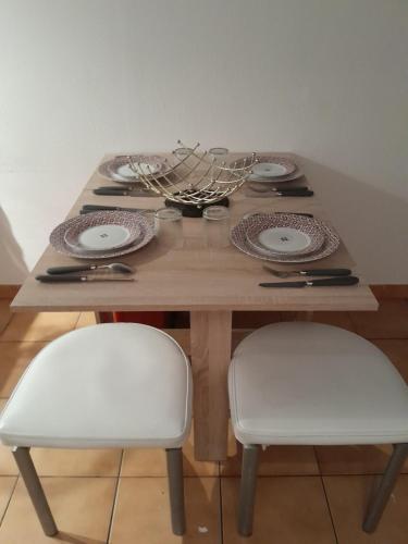 une table en bois avec deux chaises blanches et une table avec des assiettes dans l'établissement appartement city 2 d'Amiens, à Amiens