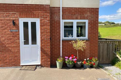 a brick house with pots of flowers and a white door at The Burrow Devon in Longdown