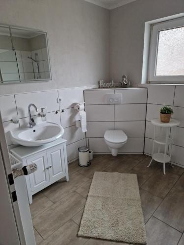W łazience znajduje się umywalka, toaleta i lustro. w obiekcie Ferienwohnung Nordseetraum w mieście Hage