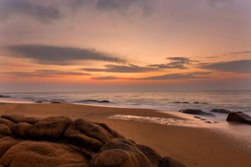 a beach with rocks in the sand at sunset at Uga Chena Huts - Yala - All Inclusive in Yala