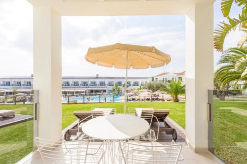 un patio con una mesa y sillas blancas y una sombrilla en MarSenses Paradise Club, en Cala'n Bosch