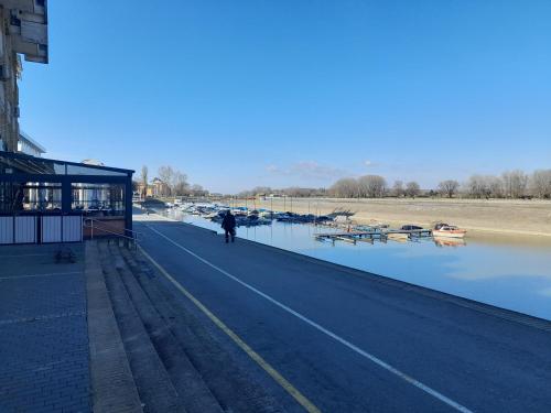 a person walking down a road next to a river with boats at Koleos in Osijek