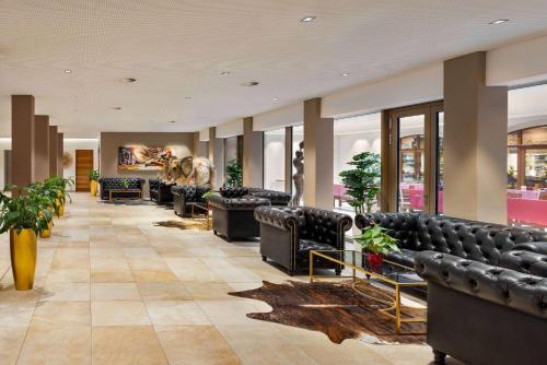 eine Lobby mit schwarzen Ledersofas und Pflanzen in der Unterkunft Amedia Plaza Dresden, Trademark Collection by Wyndham in Dresden