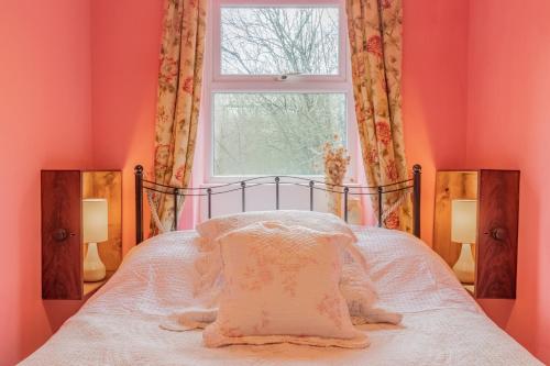 a bedroom with pink walls and a bed with a window at Millpond Cottage in Holmfirth