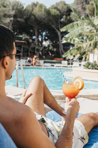 a man sitting next to a pool with a drink at Hotel Xaloc Playa in Punta Prima