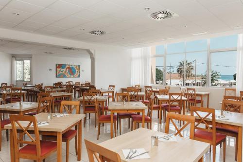 ein Restaurant mit Holztischen, Stühlen und Fenstern in der Unterkunft Hotel Xaloc Playa in Punta Prima