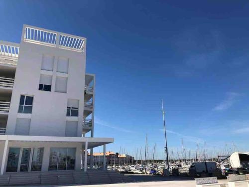 a white building next to a marina with boats at Les Voiles Blanches T2 luxe à 100m de la plage in Leucate