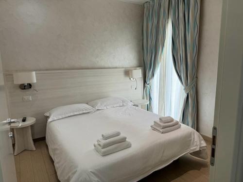 una camera da letto con un letto bianco e asciugamani di Marina Beach Aparthotel a Rimini