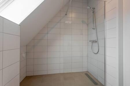 a bathroom with a shower in a white tile wall at Hello Zeeland - Vakantiewoning Knuitershoek 88 in Kloosterzande