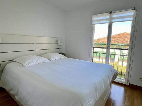 Cette chambre comprend un lit blanc et une grande fenêtre. dans l'établissement Confort à Cambo : T2 pour 2 pers., balcon-terrasse, cuisine équipée, parking, accès internet - FR-1-495-133, à Cambo-les-Bains