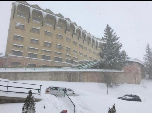 un edificio en la nieve con coches aparcados delante en villa aremogna, en Roccaraso