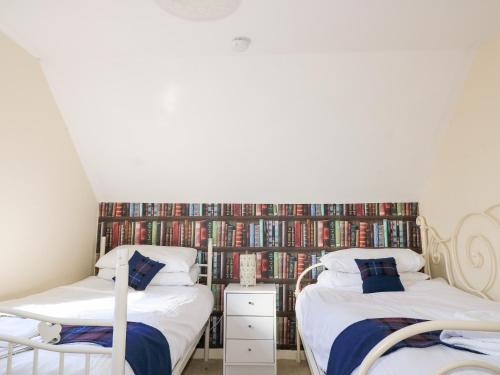 two beds in a room with a wall of books at Hidden House Hebrides in Garrabost