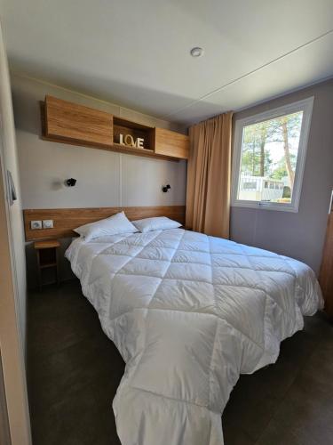 un grand lit blanc dans une chambre avec une fenêtre dans l'établissement Jolie Mobil home 2 chambres (198), à Saint-Jean-de-Monts