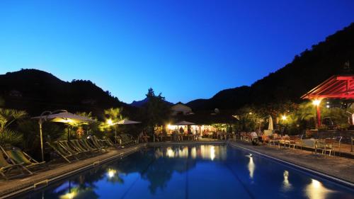 una piscina por la noche con sillas y sombrillas en Glamping Italian Riviera, en Isolabona