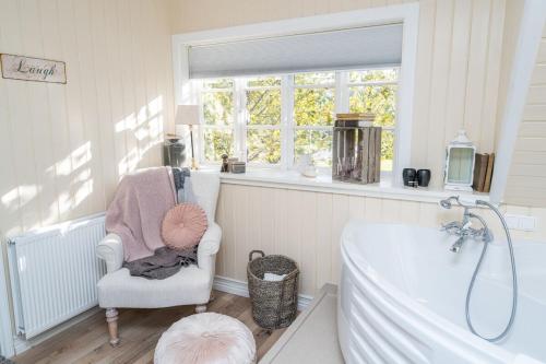 baño con bañera, silla y ventana en SKYR Guest House, en Hveragerði