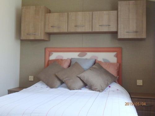 een slaapkamer met een wit bed en houten kasten bij Caravan 82, Vaenol in Tywyn