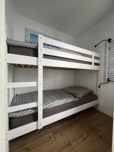 2 białe łóżka piętrowe w pokoju z drewnianą podłogą w obiekcie Ostseeliebe M-5-6 w mieście Heiligenhafen