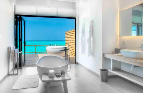 a white bathroom with a tub and a sink at Fushifaru Maldives with 50 percent off on sea plane roundtrip 04 nights & above in Fushifaru