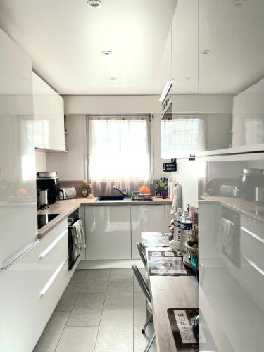 une cuisine avec des armoires blanches et une table à l'intérieur dans l'établissement Appartement 3 pièces 70m² Courbevoie Paris La Défense avec Balcon, à Courbevoie