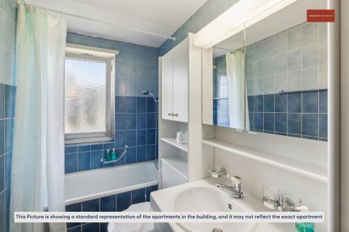 a blue tiled bathroom with a sink and a window at Urban Living Redefined: Apartment in Oerlikon in Zürich