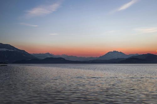 a sunset over the water with mountains in the background at ARISER - Zug City View 1 Business Apartment in Zug