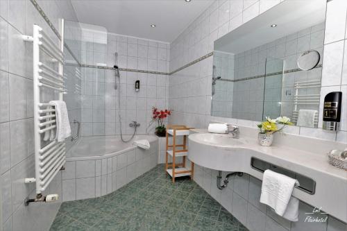 a white bathroom with a tub and a sink and a bath tub at Flairhotel am Wörthersee in Velden am Wörthersee