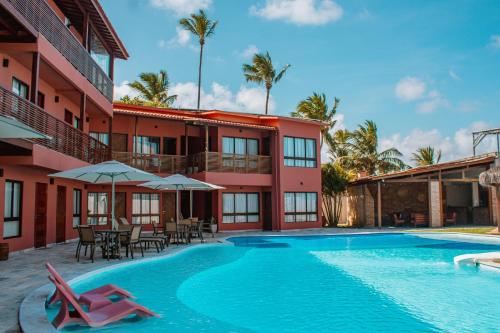 a resort with a swimming pool and chairs and a building at Pousada Un Paso del Mar in Porto De Galinhas
