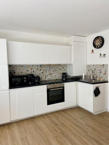 une cuisine avec des placards blancs et une horloge murale dans l'établissement Grands studio en bord de mer, à Cagnes-sur-Mer