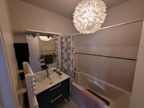 La salle de bains est pourvue d'un lavabo, d'une baignoire et d'un lustre. dans l'établissement Apparte Cosy Avec Terrasse Et Parking, à Dinan