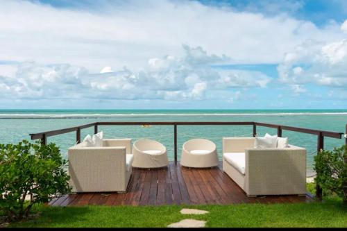 una terraza con sillas blancas y vistas al océano. en Flat beira mar no Manihi - Muro Alto, en Ipojuca