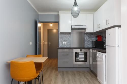 une cuisine avec des armoires blanches et une table et des chaises en bois dans l'établissement Appartement confortable Proche de Paris - Balcon - Parking & Wifi, à Argenteuil