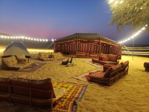 uma tenda com sofás e cadeiras no deserto em Enjoy The Leisure of Overnight Campsite in Dubai Desert Safari With Complementary Pick up em Dubai