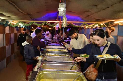 een groep mensen die bij een buffet staan met eten bij Enjoy The Leisure of Overnight Campsite in Dubai Desert Safari With Complementary Pick up in Dubai