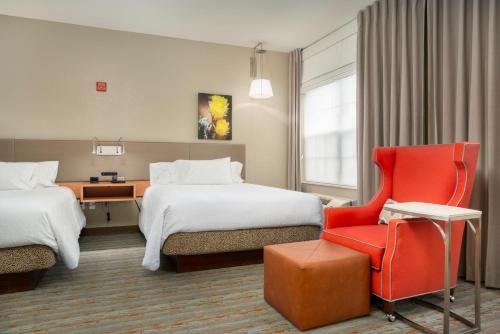 Cette chambre d'hôtel comprend deux lits et un fauteuil rouge. dans l'établissement Hilton Garden Inn Phoenix Airport, à Phoenix