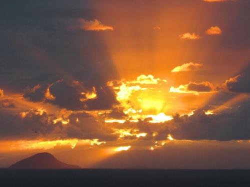 a sunset with the sun shining through the clouds at Bangalô Ilhabela in Ilhabela